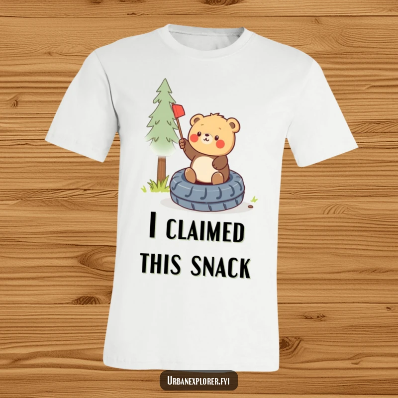 Funny round bear cub triumphantly planting a small flag on a discarded tire, printed on a fun t-shirt.